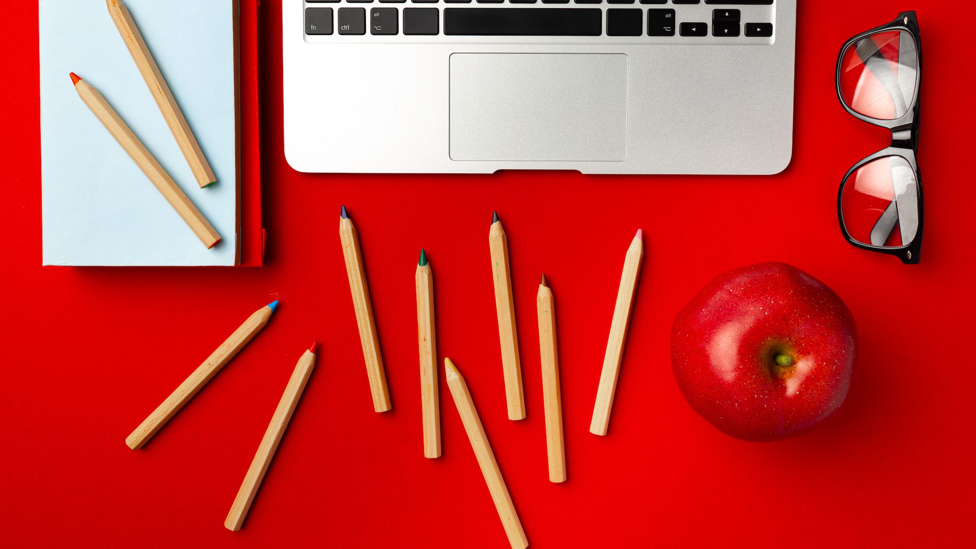Top view of student working space with open laptop and red apple, other supplies